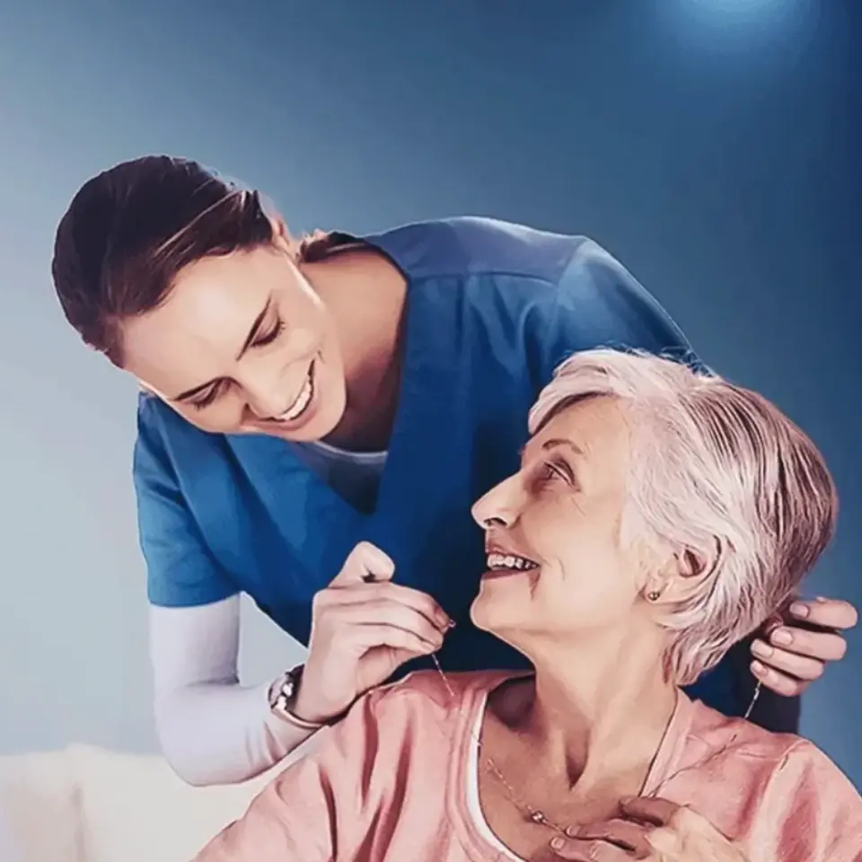 Cuidadora de uniforme azul acolhendo uma senhora idosa sorridente